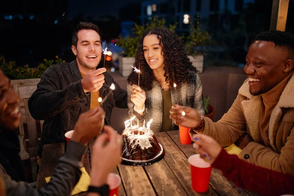 Grupo de diversos adultos jóvenes sentados en la azotea temática boho fiesta iluminación chispas de pastel de cumpleaños. — Foto de Stock