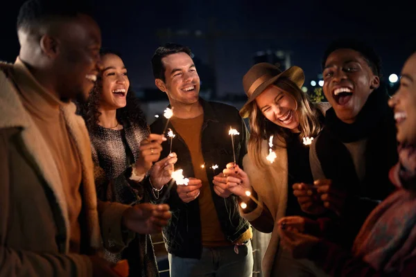 Diverso grupo de amigos riendo en una fiesta en una terraza en la azotea. La vida nocturna en la ciudad, Iluminación Sparklers — Foto de Stock