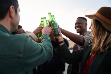 Çok kültürlü bir grup genç yetişkin kadeh kaldırıyor ve şehirdeki bir terasın balkonunda içkilerle gülüyor.. 