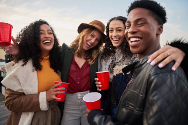 Kameraya gülümserken eğlenen farklı arkadaş gruplarının portresi. Akşamları çatıdaki terasta gülüp sosyalleşiyorlar.