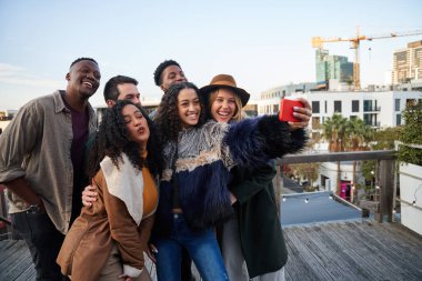 Çok kültürlü bir arkadaş grubu çatıdaki bir partide selfie çekiyor. Genç yetişkin arkadaşlarla poz vermek..
