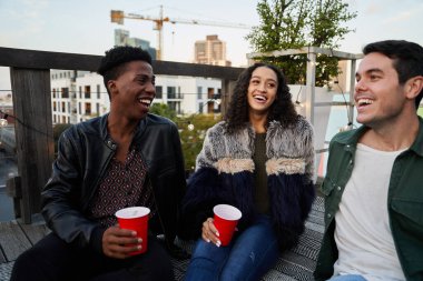 Birbirine gülümseyen bir grup çok kültürlü genç yetişkin. Şehirdeki bir çatı partisinde, güzel zamanlardı..