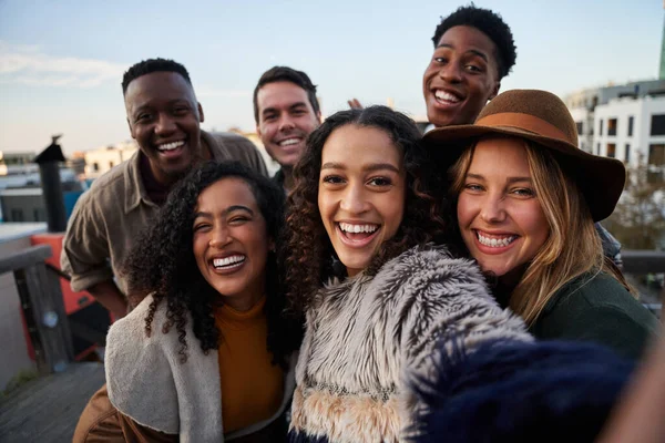 Groupe multiculturel d'amis prenant un selfie lors d'une fête sur le toit. Gros plan, sourires avec divers jeunes adultes. — Photo