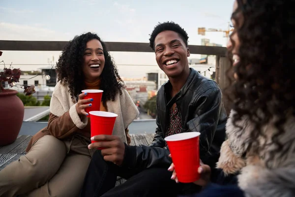 一群快乐的多文化年轻人坐在楼顶的阳台上社交、喝酒、笑 — 图库照片