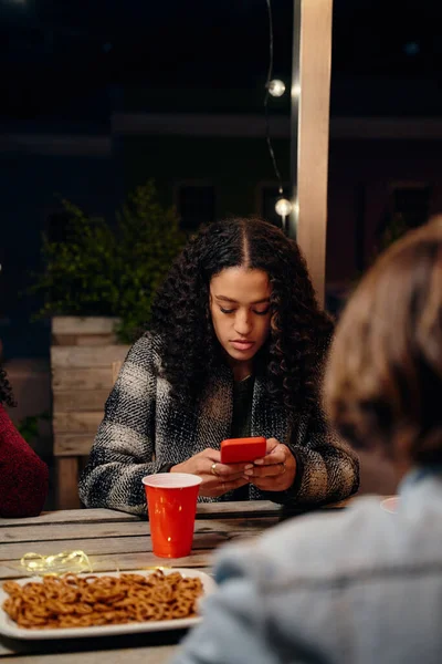 Biracial young adult female sitting at a party, texting on her phone. Anti-social, using technology at rooftop party — Stock Photo, Image