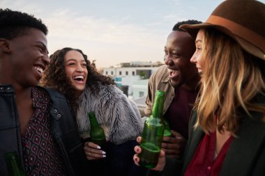 Çok kültürlü genç yetişkinlerden oluşan bir grup şehrin çatı terasında birlikte gülüyorlar. Arkadaşlarınla gülümse..