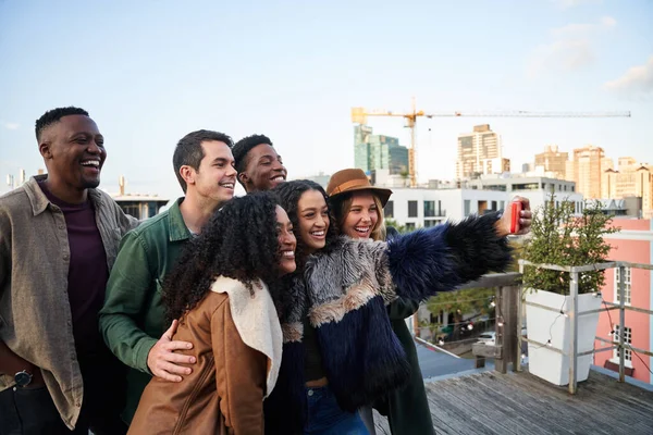 Groupe multiculturel d'amis prenant un selfie lors d'une fête sur le toit. Sourire avec fond de paysage urbain. — Photo