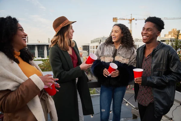 不同的一群朋友站在城市的屋顶平台上，在晚上与朋友们一起欢笑和社交 — 图库照片