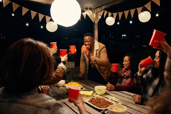 Hombre negro de pie, haciendo un brindis en la fiesta en la azotea con un grupo de amigos diversos en una fiesta al aire libre —  Fotos de Stock