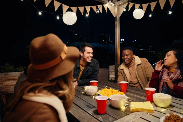 Groupe multiculturel de jeunes amis adultes riant autour d'une table lors d'une fête branchée sur le toit. Manger et boire, s'amuser — Photo