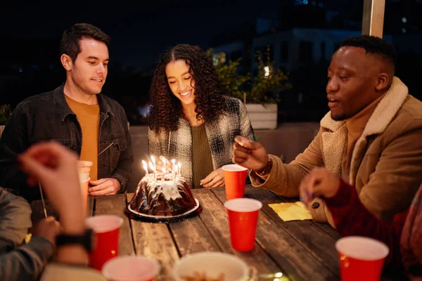 一群不同的年轻人坐在时髦的屋顶派对上，用生日蛋糕点亮火花. — 图库照片