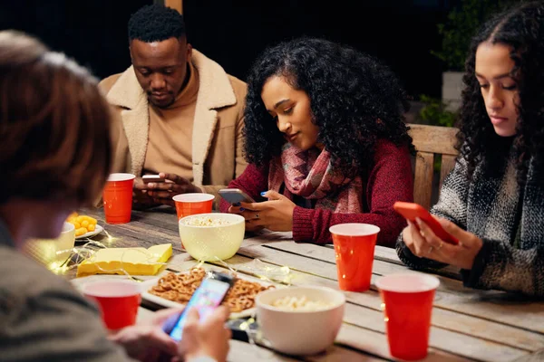 Groupe de divers jeunes amis adultes assis autour de la table à la fête tous sur leurs téléphones, étant antisocial. — Photo