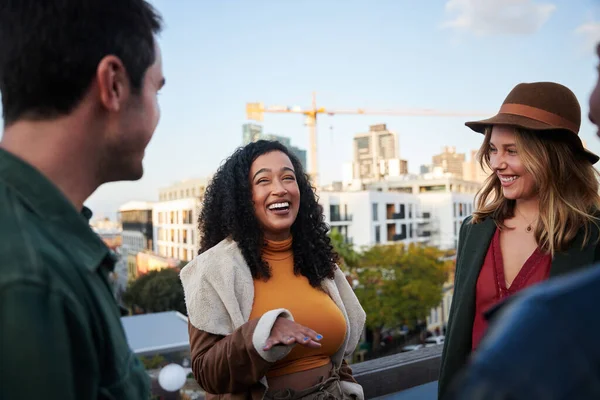 Біреальна жінка сміється з групою багатокультурних друзів, які спілкуються на терасі на даху в сутінках . — стокове фото