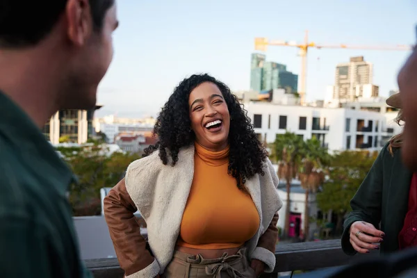 Mujer Biracial riendo, pasando un buen rato con un grupo de amigos multiculturales socializando en una terraza en la azotea al atardecer. —  Fotos de Stock