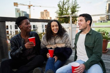 Çok kültürlü genç yetişkinler birlikte şakaya gülüyorlar. Şehirdeki bir çatı partisinde oturmak, güzel zamanlardı..