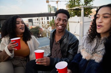 Çatı terasında oturmuş sosyalleşen, içen ve gülen çok kültürlü genç yetişkinlerden oluşan canlı bir grup.