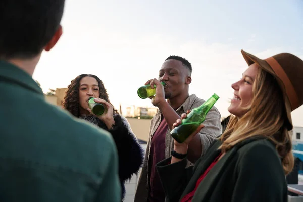 Groupe multiculturel de jeunes adultes riant avec boissons sur le balcon d'un toit-terrasse de la ville. — Photo