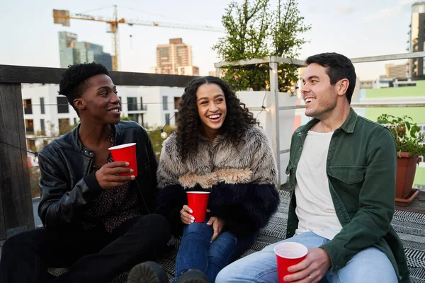 Çok kültürlü genç yetişkinler birlikte şakaya gülüyorlar. Şehirdeki bir çatı partisinde oturmak, güzel zamanlardı..