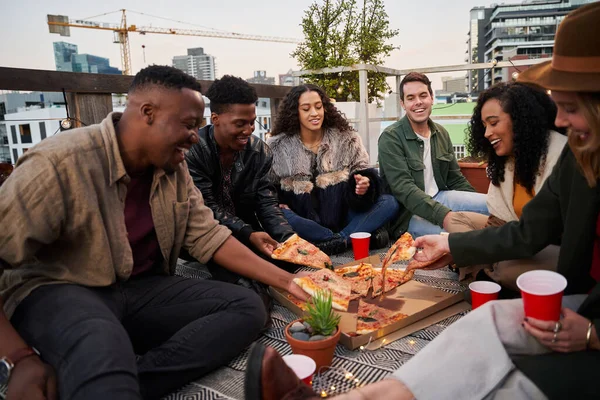 Groupe d'amis divers attrapant des morceaux de pizza à manger tout en étant assis sur le toit-terrasse dans la ville — Photo