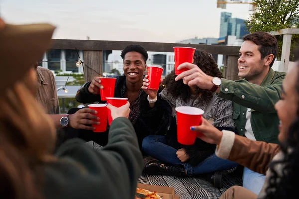 Gruppe verschiedener Freunde prostet sich mit roten Tassen auf Dachterrasse in der Stadt zu und amüsiert sich — Stockfoto