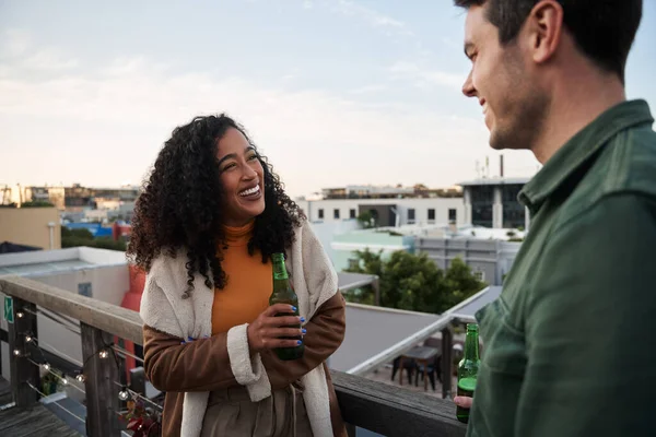 Biracial jeune femme adulte riant avec un ami sur le balcon d'un toit-terrasse dans la ville. Boisson à la main, vue sur le paysage urbain — Photo