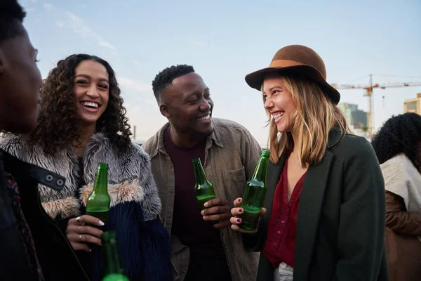 Gruppo di giovani adulti multiculturali che ridono insieme su una terrazza panoramica della città. Bevande in mano, sorrisi con gli amici. — Foto Stock