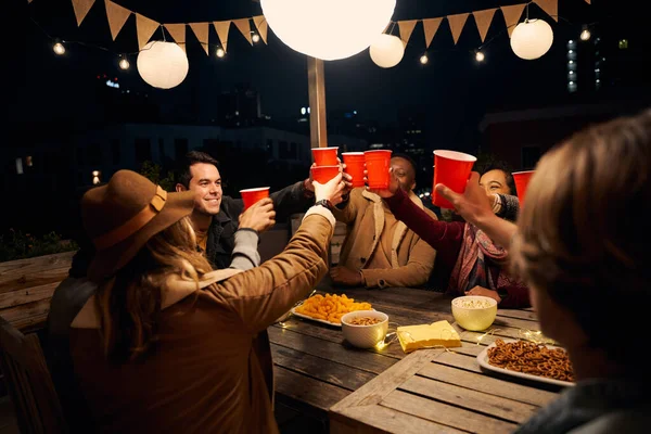 Groupe d'amis divers assis, faire un toast à une fête en plein air autour d'une table à thème boho. Tasses rouges et rires — Photo