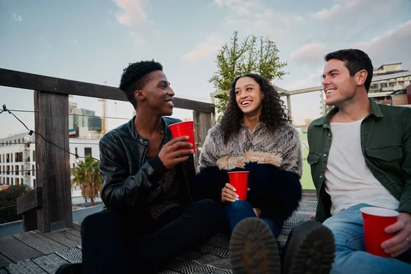 Grupo de jóvenes adultos multiculturales en una fiesta en la azotea de la ciudad. Buenos tiempos, sonriéndose el uno al otro. —  Fotos de Stock