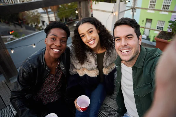 Selfie çekerken gülümseyen bir grup çok kültürlü genç yetişkin. Şehirdeki bir çatı partisinde, güzel zamanlardı..