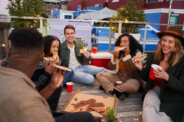 成群结队的多文化青年朋友坐在城市的屋顶上吃披萨. — 图库照片