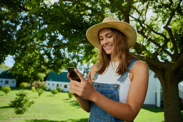 Femme agricultrice caucasienne souriant tout en envoyant des SMS sur un appareil cellulaire — Photo