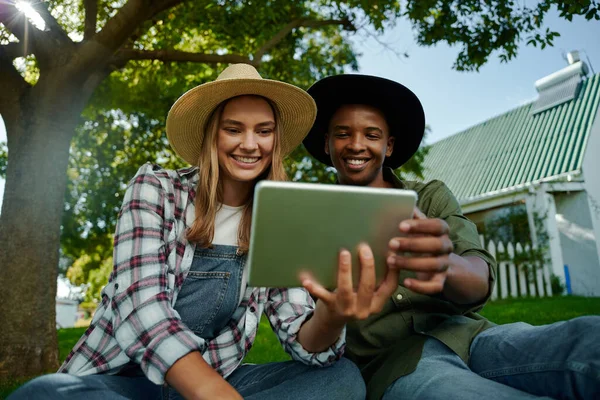 Raça mista masculino e feminino famers sentados juntos na grama verde olhando para tablet digital — Fotografia de Stock