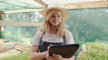 Serada çalışan beyaz kadın çiftçi elinde dijital tabletle meslektaşına gülüyor.