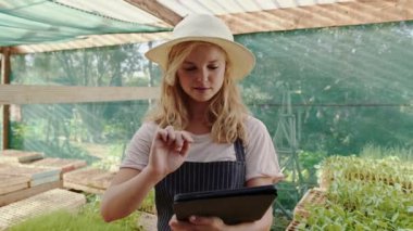 Yeşil evde çalışan beyaz kadın çiftçi dijital tablet üzerinde yazı yazıyor.