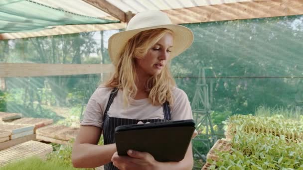 Blanke vrouwelijke boer werkt in een groene huis dragen strohoed typen op digitale tablet — Stockvideo
