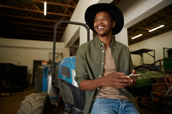 Smiling mixed race male farmer sitting on tractor texting on cellular device — Stock Photo, Image