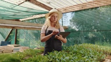 Beyaz kadın serada çalışıyor. Dijital tablet üzerinde yazıyor.