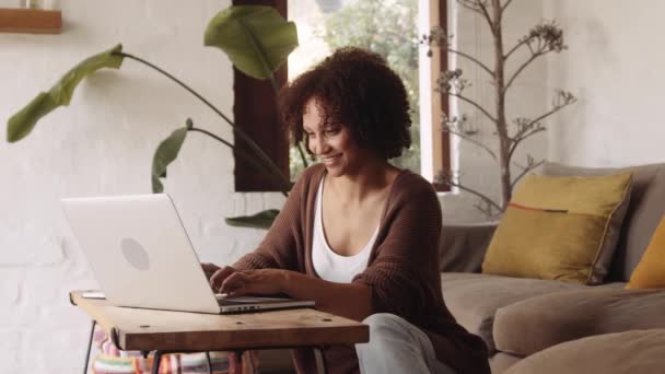 Двухсторонняя женщина улыбается, работая из дома на ноутбуке в современной гостиной днем — стоковое видео