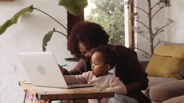 आधुनिक शैली के लिविंग रूम में बाइरासियल महिला और छोटे बच्चे बच्चे को अपने लैपटॉप पर टाइप करने की अनुमति देता है . — स्टॉक वीडियो