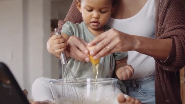 La mamma di nascita cuoce insieme alla sua giovane figlia, seguendo la ricetta su tavoletta elettronica nella cucina in stile moderno, rompendo uova e sbattendo.. — Video Stock