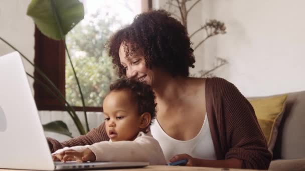 Trabajo desde el hogar madre biracial y el niño pequeño en la sala de estar de estilo moderno durante el día, jugando en el ordenador portátil. — Vídeos de Stock