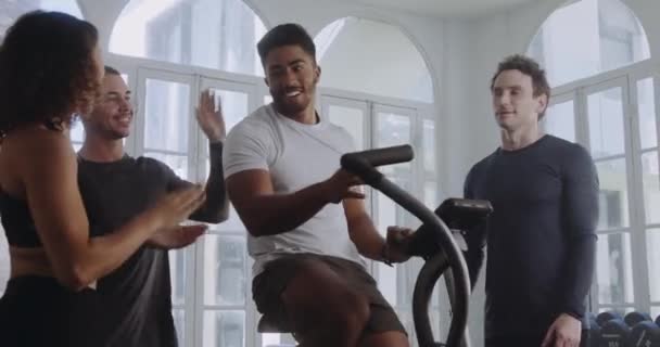 Sexo masculino biracial comemorando com os amigos depois de se exercitar na bicicleta em um ginásio de estilo moderno. — Vídeo de Stock