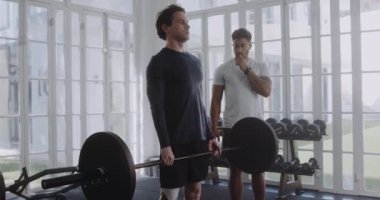 Modern tarz spor salonunda antrenörle birlikte protez bacağı olan beyaz bir erkek. Ağırlık kaldırmak ve sıkı çalışmak..