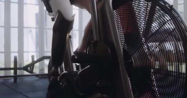 Белый мужчина с протезной ногой катается на велосипеде. Спортсмен-инвалид, тренирующийся в современном спортивном зале. — стоковое видео