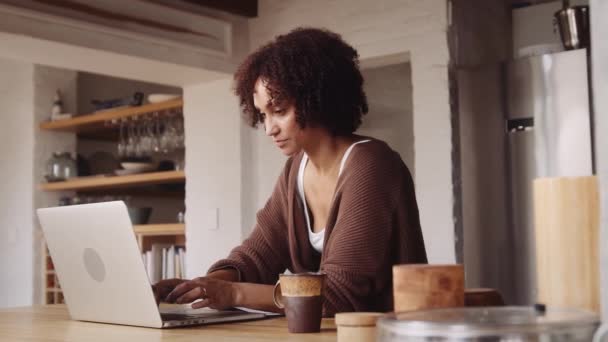 Mãe biracial estressada trabalhando no laptop e fazendo anotações em casa na cozinha moderna. — Vídeo de Stock