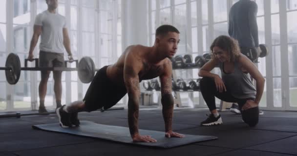 Jonge volwassen blanke man doet oefeningen op mat met zijn trainer in een moderne fitnessruimte. Hi-5 viering. — Stockvideo