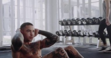 Modern tarz spor salonunda dövmeleri olan odaklanmış beyaz bir erkek oturma egzersizi yapıyor..