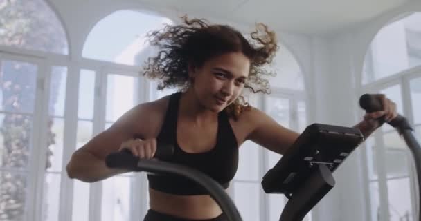 Donna di nascita che lavora sodo sulla air bike in una palestra in stile moderno. Fitness e stile di vita sano. — Video Stock