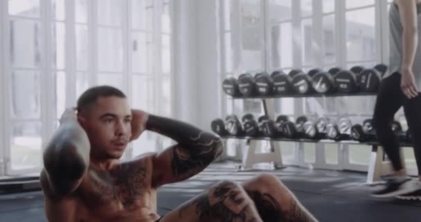 Focalisé mâle caucasien avec des tatouages dans la salle de gym de style moderne occupé finissant un exercice assis. — Video