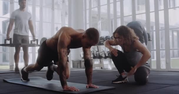 Jonge volwassen blanke man doet oefeningen op mat met zijn trainer in een moderne fitnessruimte. Hi-5 viering. — Stockvideo